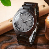 Dark wood watch with grey dial and wooden link bracelet on a wooden surface