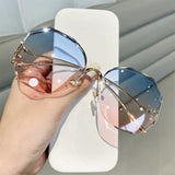 Hand holding curved sunglasses with gold frame and blue to pink gradient lens