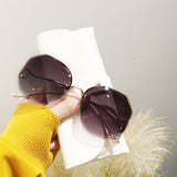 Person in yellow shirt holding curved sunglasses with dark gradient lens