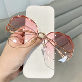 Hand holding curved sunglasses with gold frame and pink gradient lens