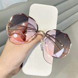 Hand holding curved sunglasses with gold frame and pink to purple gradient lens