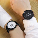 Two hands clasped together each wearing a King and Queen leather strap watch