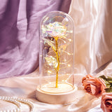 Pink galaxy rose in a glass dome with warm LED lights on a wooden base