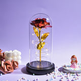 Red galaxy rose in a glass dome with warm LED fairy lights on a wooden base
