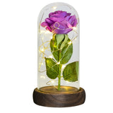 Blue foil rose with green leaves under a clear glass dome on a wooden base