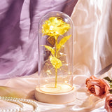 Gold foil rose with green leaves under a glass dome on a dark base