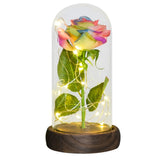 Pink foil rose with green leaves in a glass dome on a dark wooden base