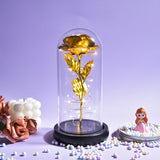 Purple foil rose with green leaves in a glass dome on a light wooden base