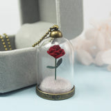 Rose terrarium glass dome pendant necklace shown close up on teal background